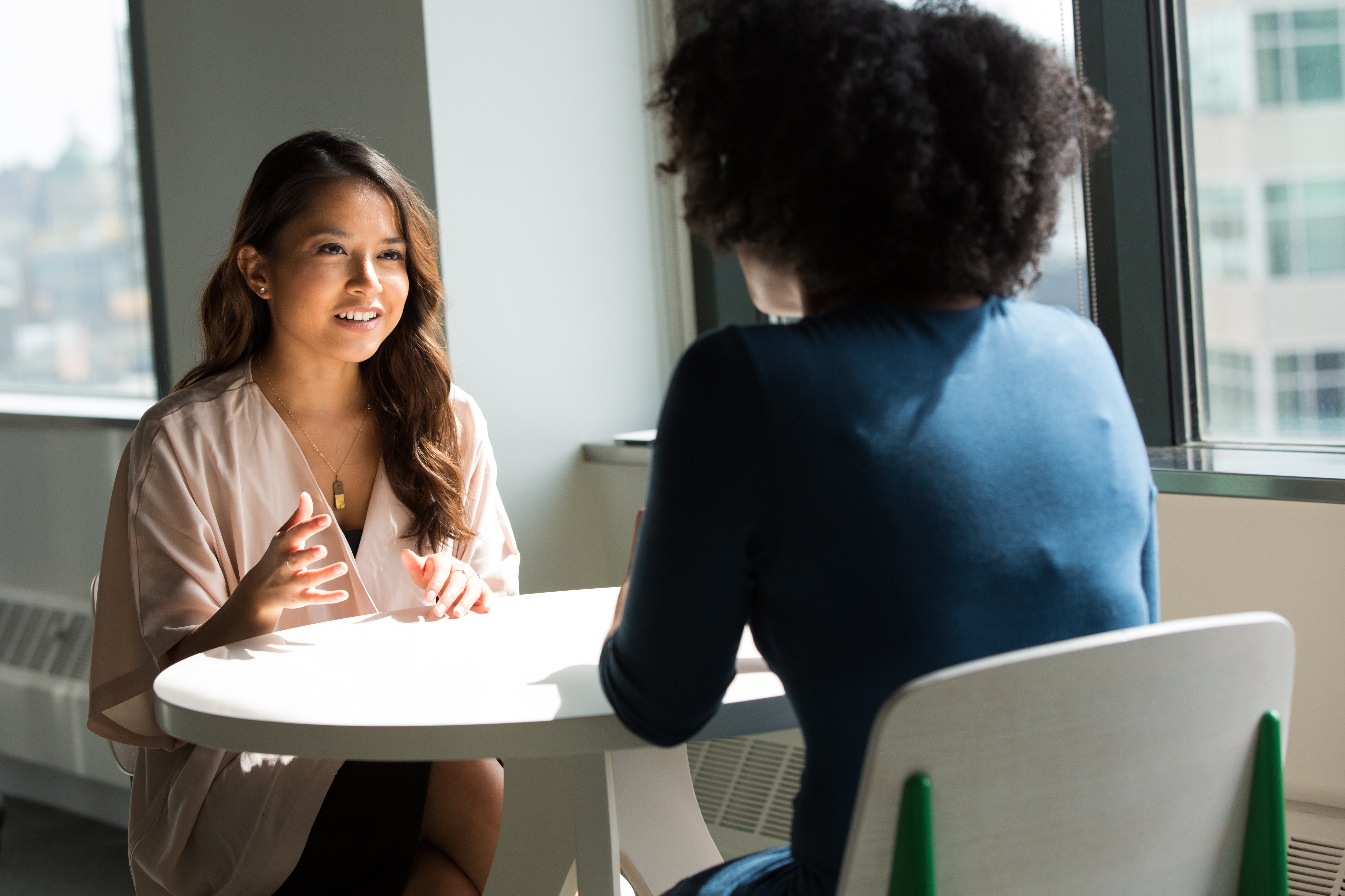Two people sit opposite each other at a table having a conversation
