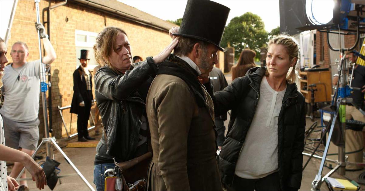 An actor dressed in a period drama costume with members of production crew adjusting his attire