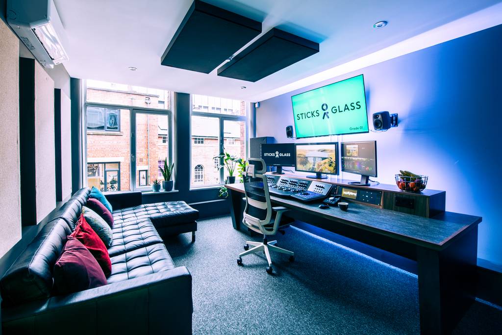 A studio space set up with a desk, a computer with 3 monitors, mixing desks and a sofa