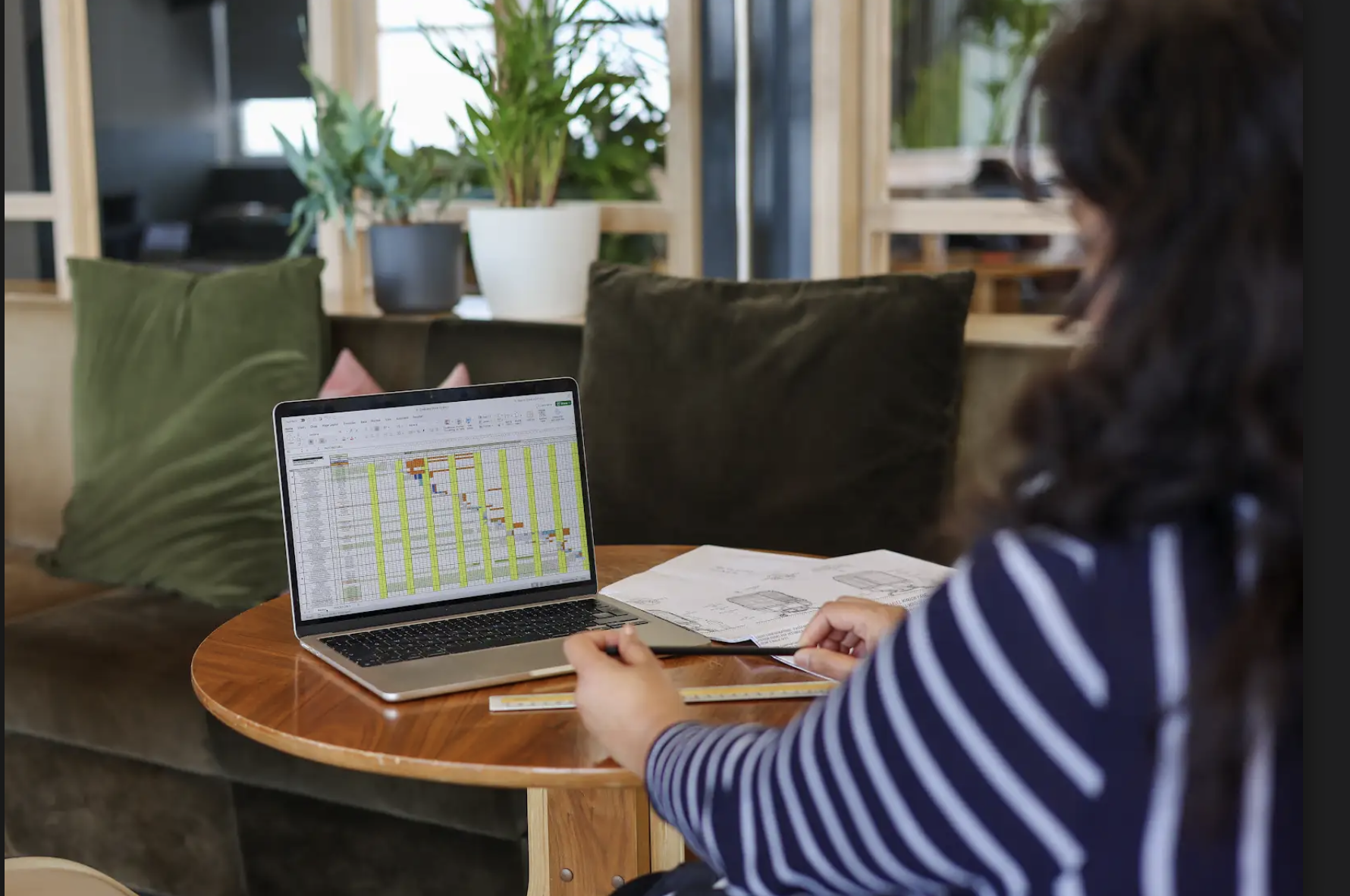 back of female typing on laptop, she has dark hair and wearing a stripey blue top.