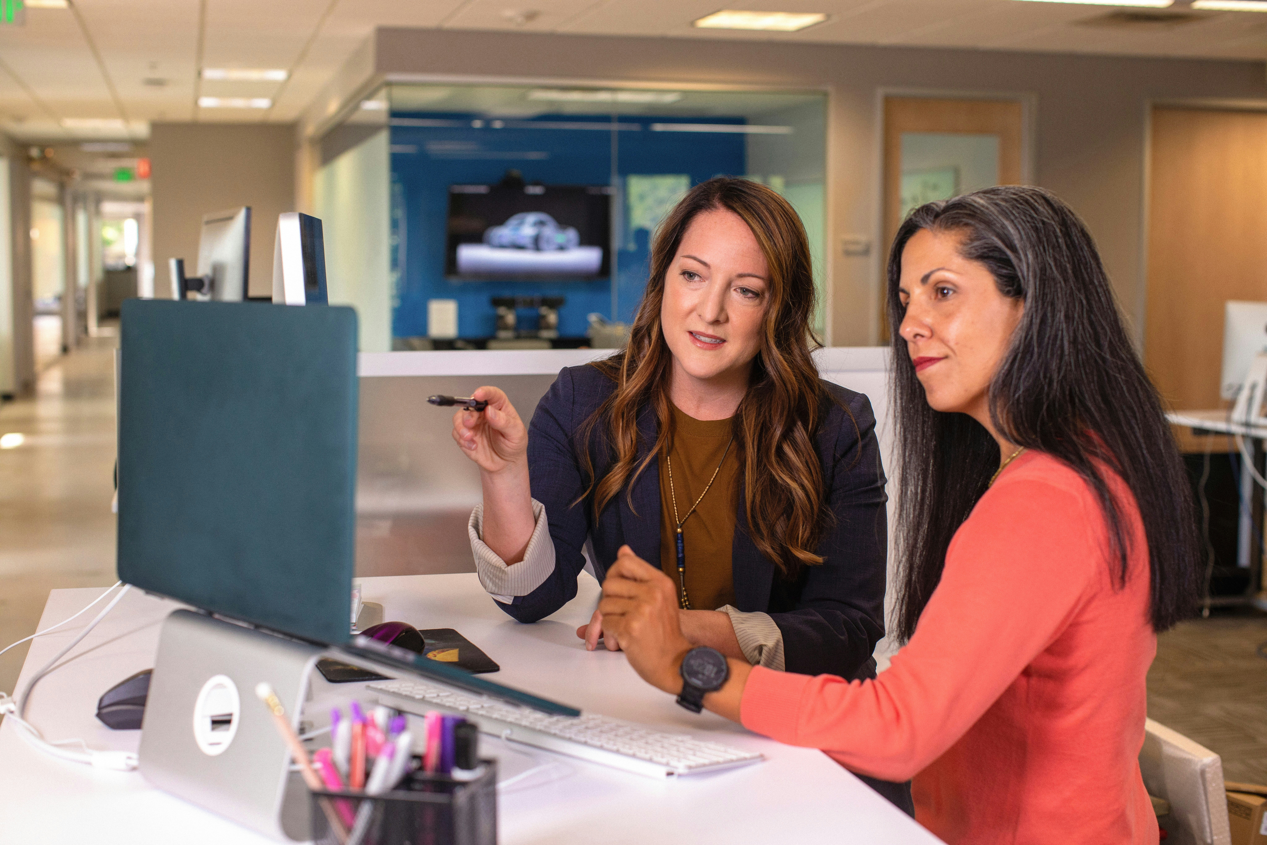 Two women sit at a desk looking together at a laptop screen