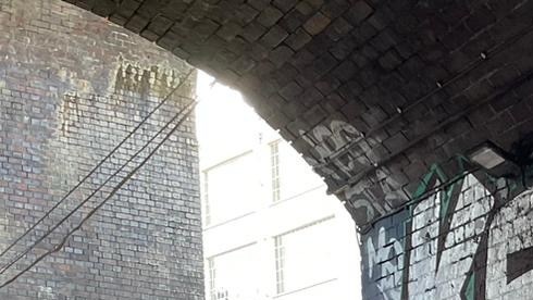 A film crew and two actors film a scene under a graffitied archway