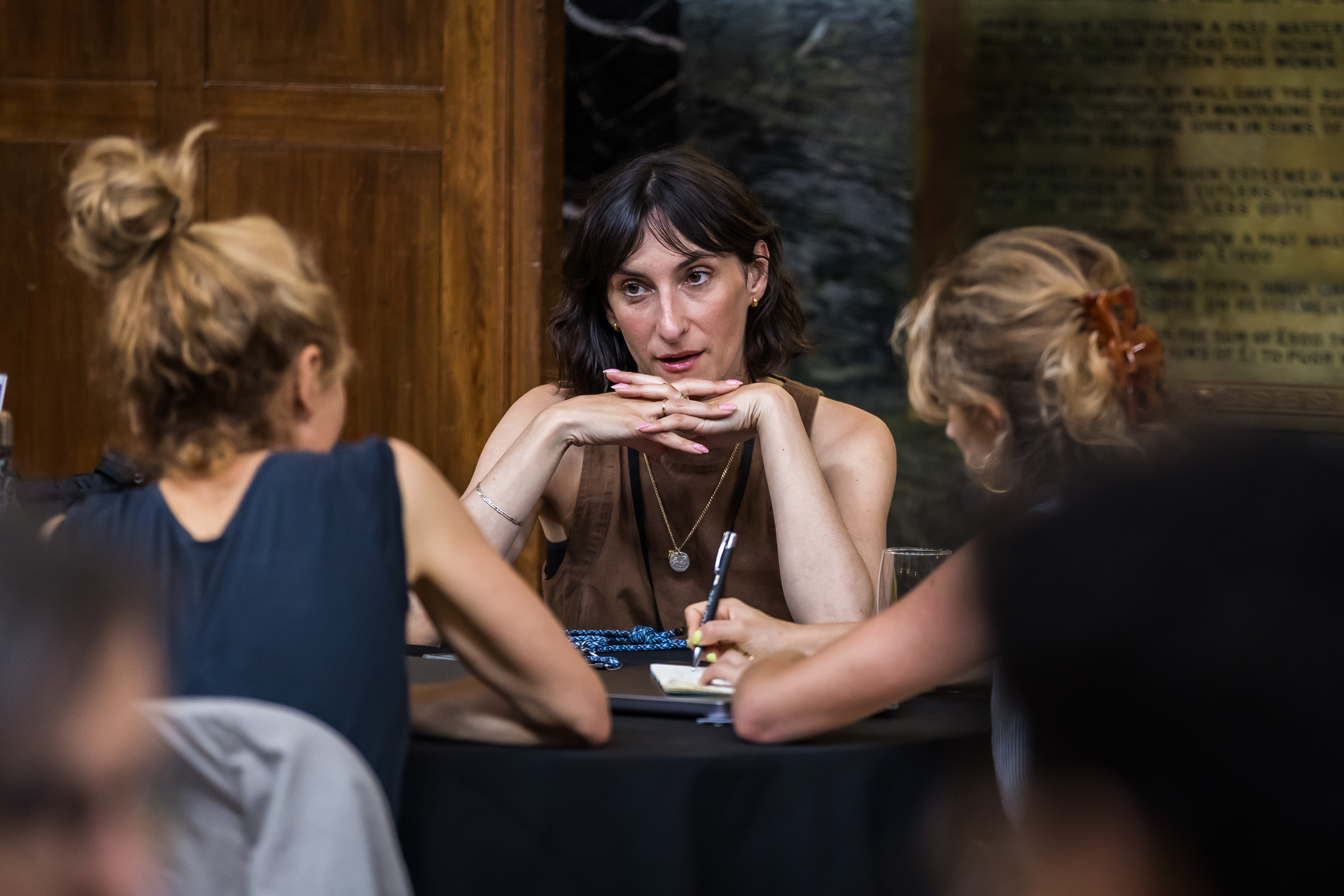Three women sat at a table at a networking event with notepads in front of them.