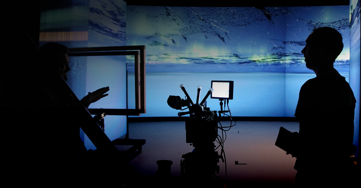 A man stands in front of a LED screen with a camera in the middle