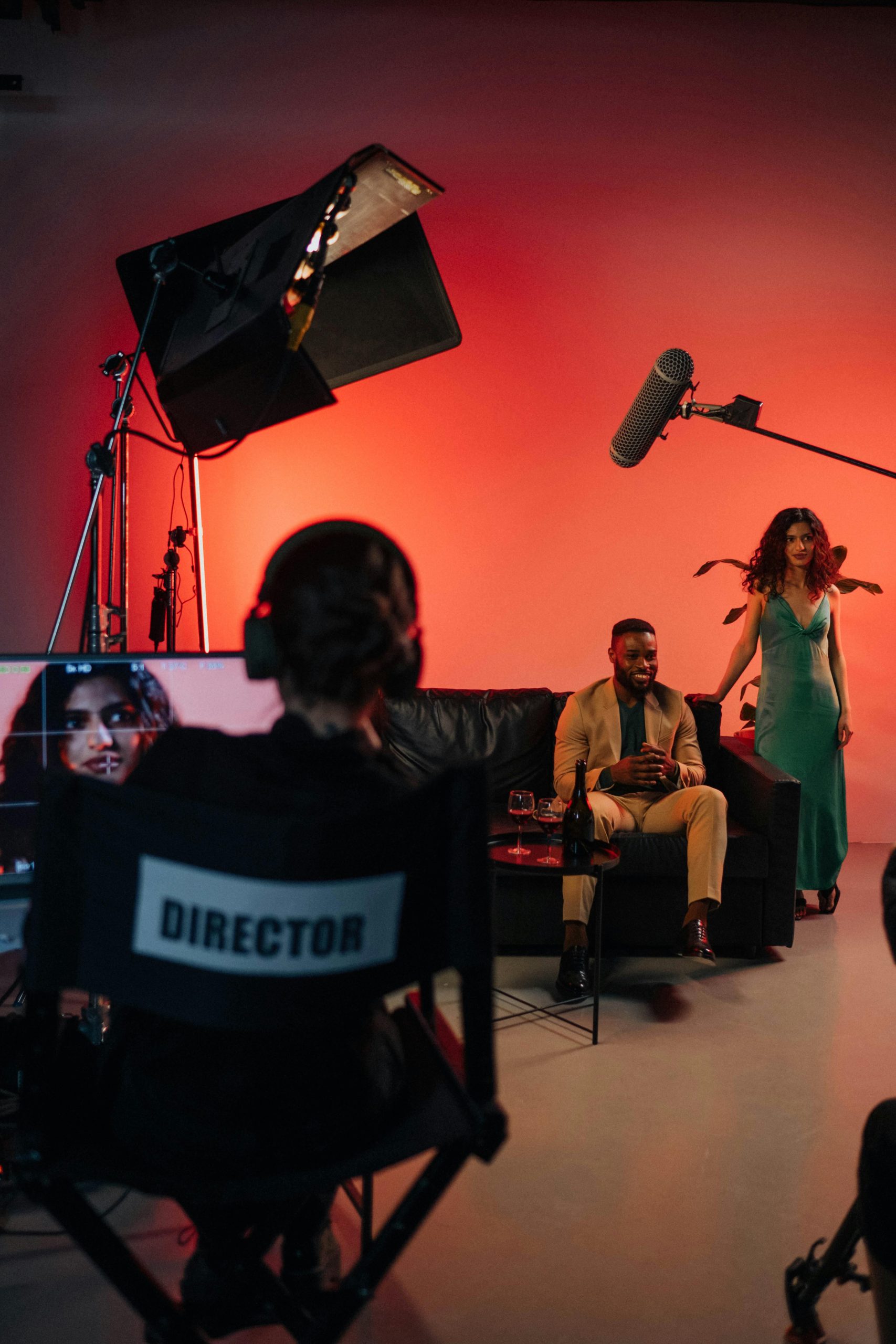 A picture of an indoor set with a orange background, actors set up around a sofa and crew holding mics and managing screen monitors.
