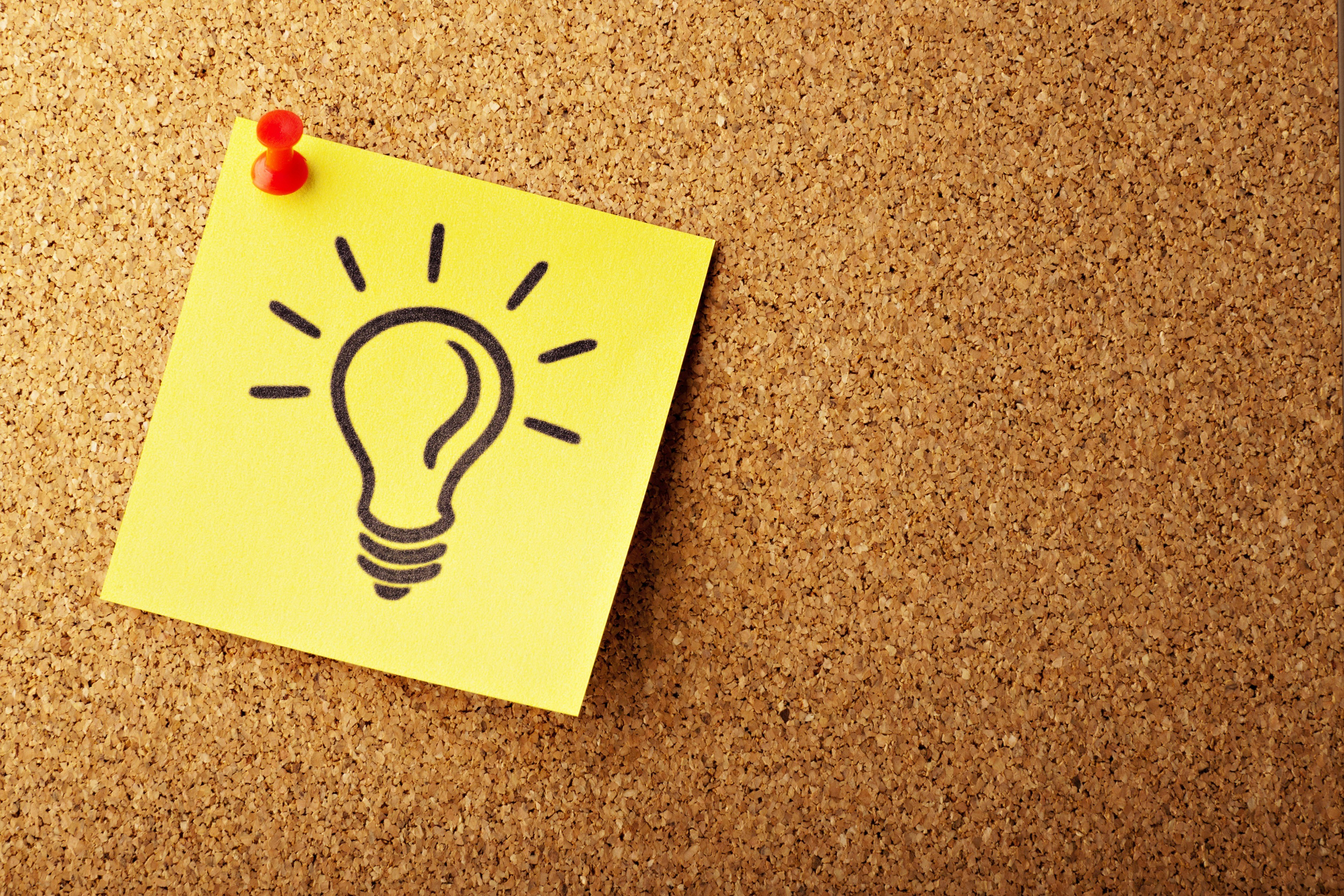 A drawing of a lightbulb on a yellow Post-It note, pinned to a brown pinboard