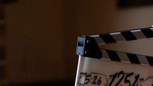Image of the two hands of a member of the production crew - with the crew member out of shot - activating a clapperboadrc