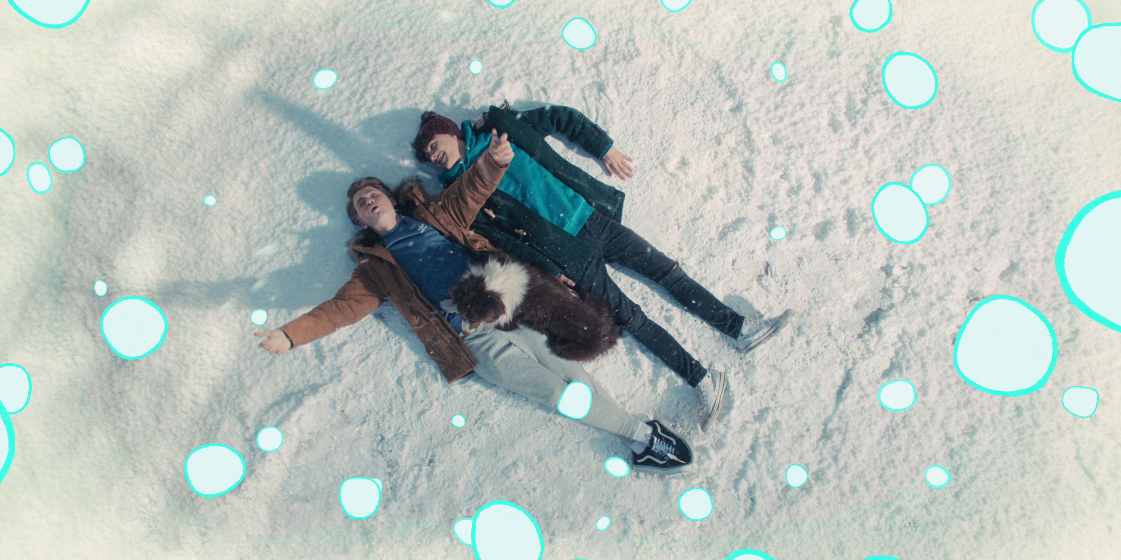image of two young teen males laying on their backs in the snow, as if about to make snow angels. The still is overlayed with animated cartoon bubbles.