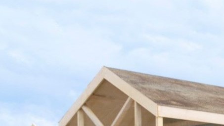 still from teh series The Beaker Girls featuring an adult woman (actress Dani Harmer) seated on a picnic table on a sandy beach alongside some wooden beach huts. She is joined by two your girls played by actresses Emma Davies and Chi-Megan Ennis-McLean